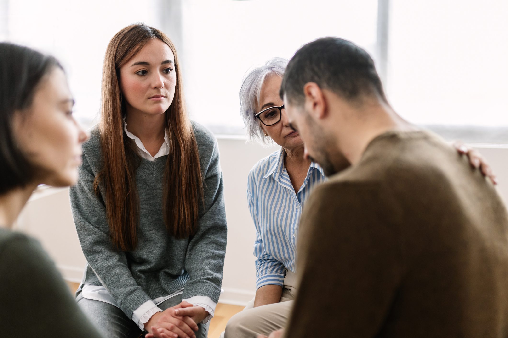 An upset man keeps his head low as he's comforted by two women in group therapy.