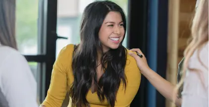 Three women engaged in conversation, smiling warmly in a professional office setting, fostering a collaborative atmosphere