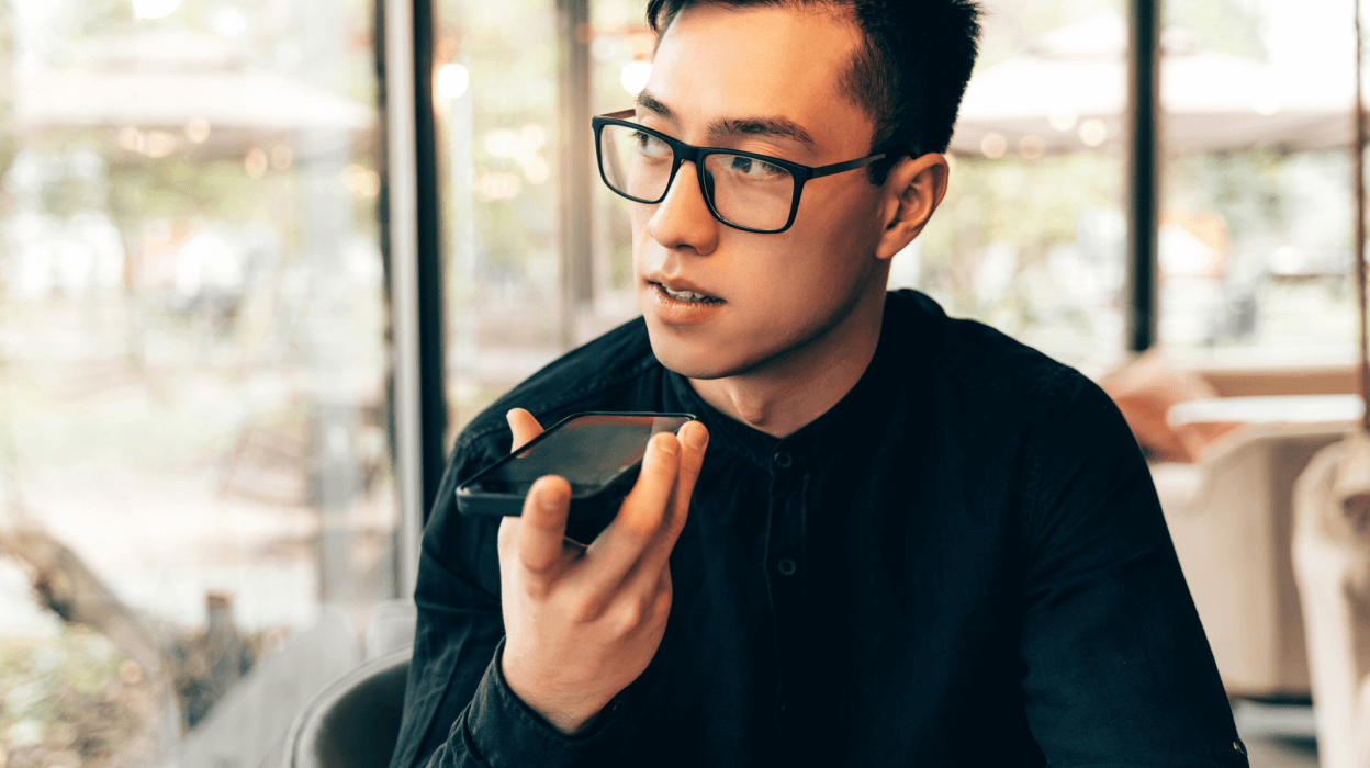 A man wearing glasses is holding a cell phone, appearing focused and engaged with the device in his hand.