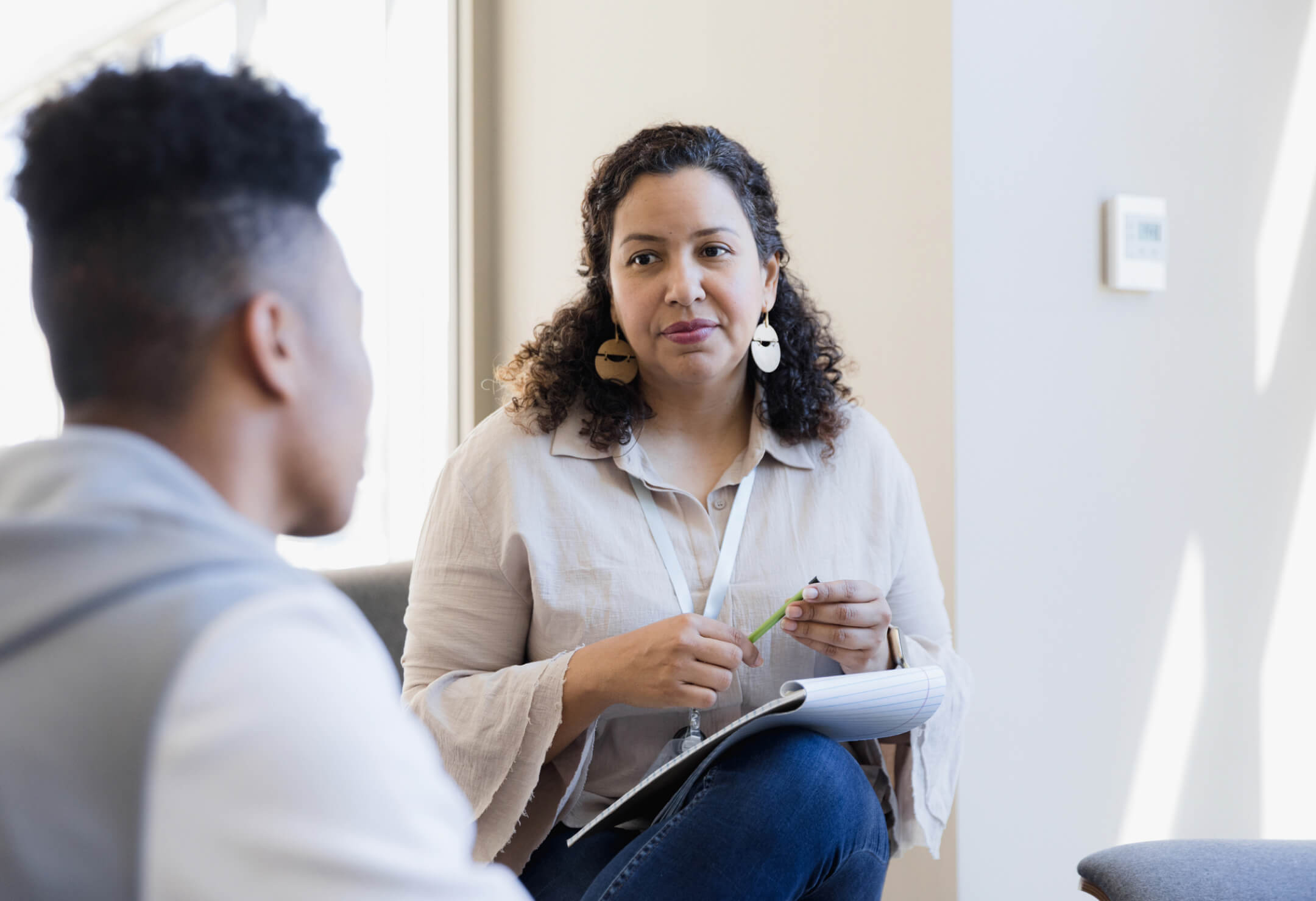 A woman engages in conversation with a man in a professional office setting, both appearing focused and attentive.