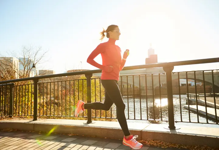 A woman jogs on a city bridge, surrounded by urban scenery and a clear blue sky, showcasing an active lifestyle
