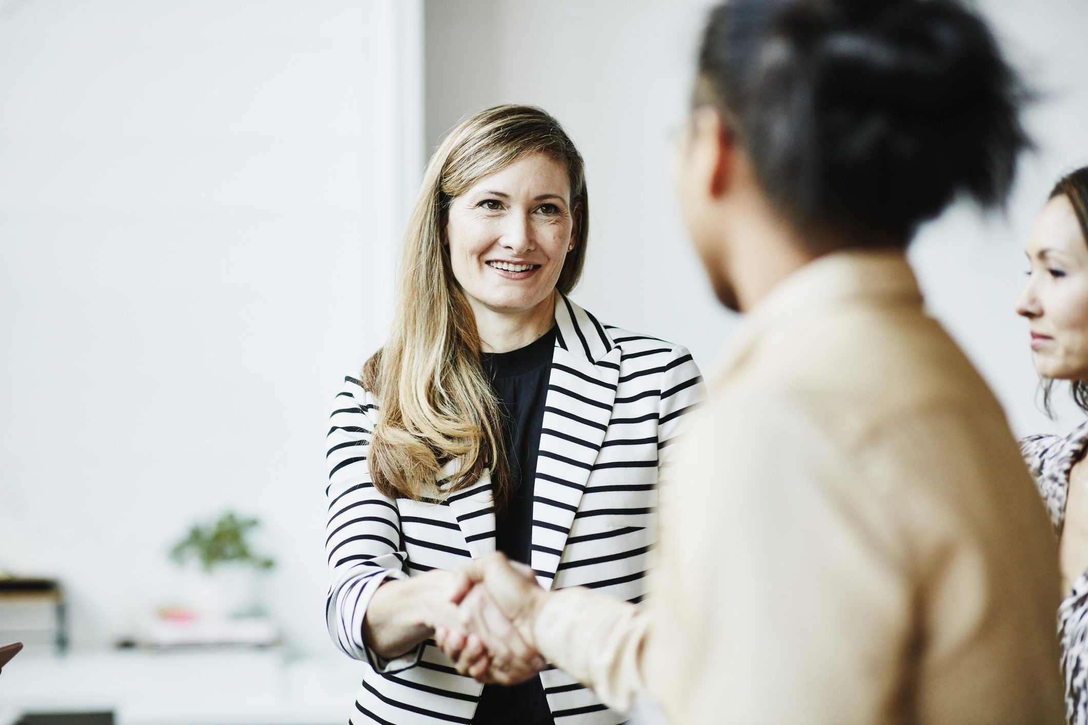 A woman and another woman shake hands in a professional office setting, symbolizing collaboration and agreement.