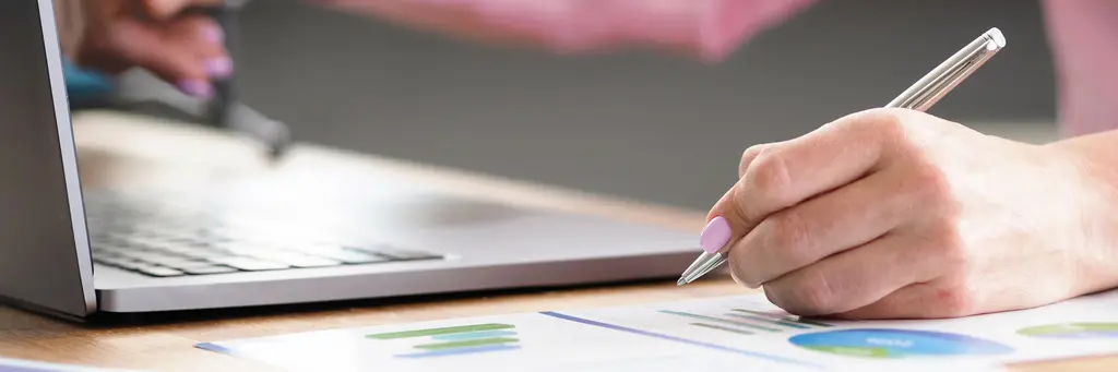A hand taking notes beside a laptop