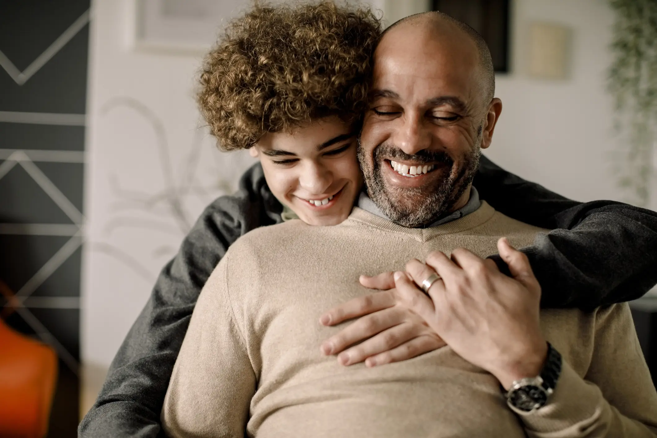 A man and his son embrace warmly in a cozy living room, showcasing a moment of love and connection between them.