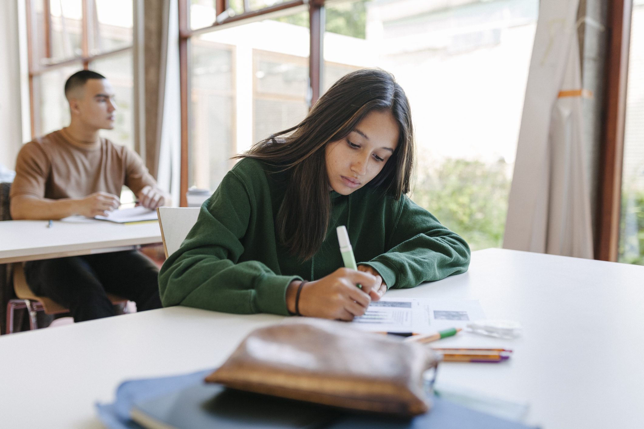 girl sitting at classroom desk, writing in a notebook