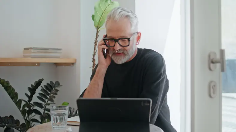 Older man looking at a computer and talking on the phone