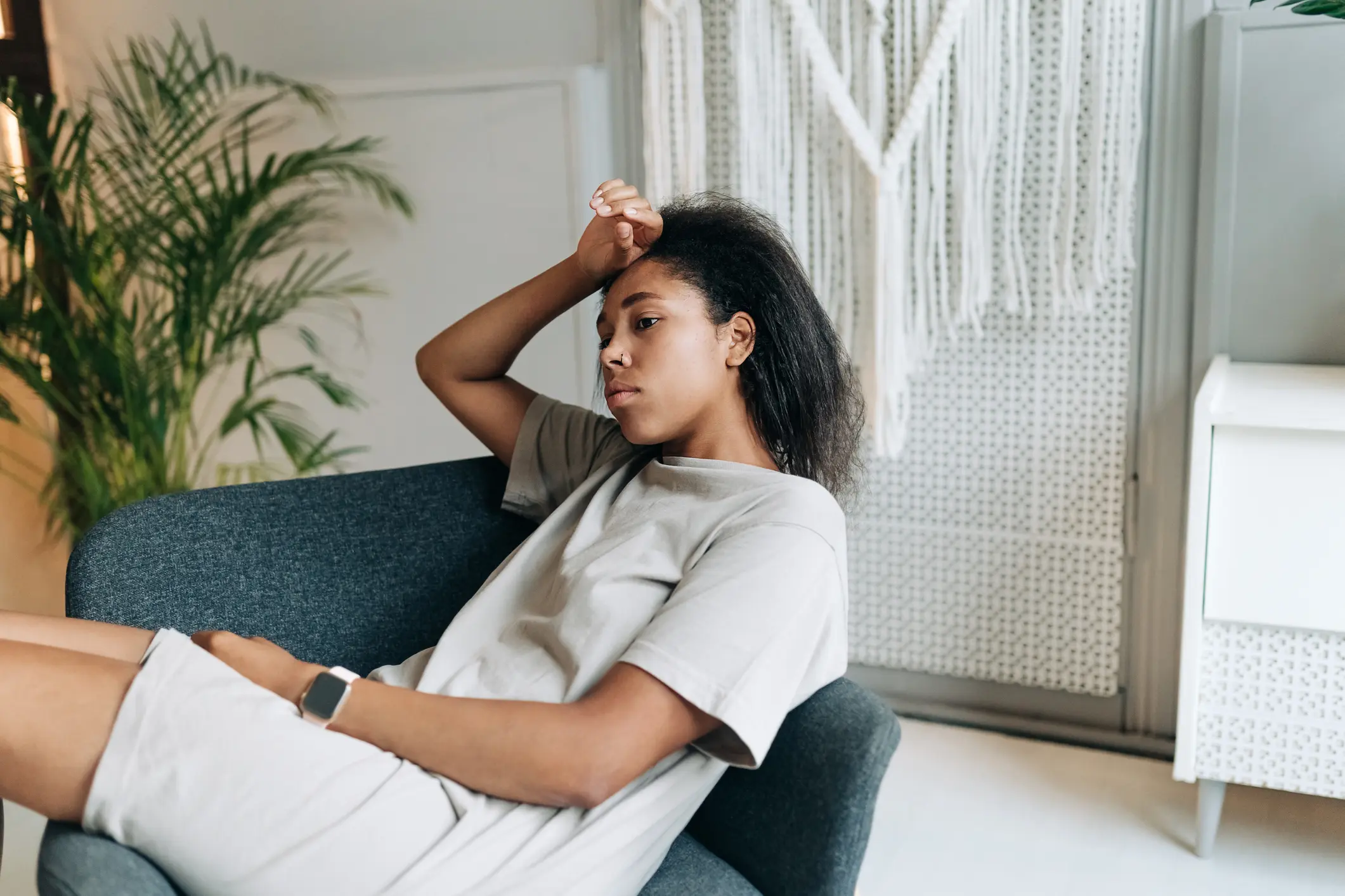 Depressed African American woman holds her hand to her temple as she lays on a blue chair